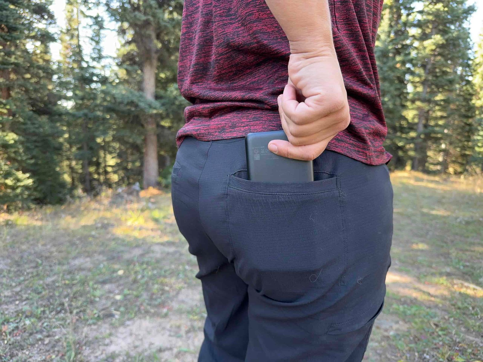 A person's hand placing a power bank into the back pocket of the Athleta Trekkie pants.