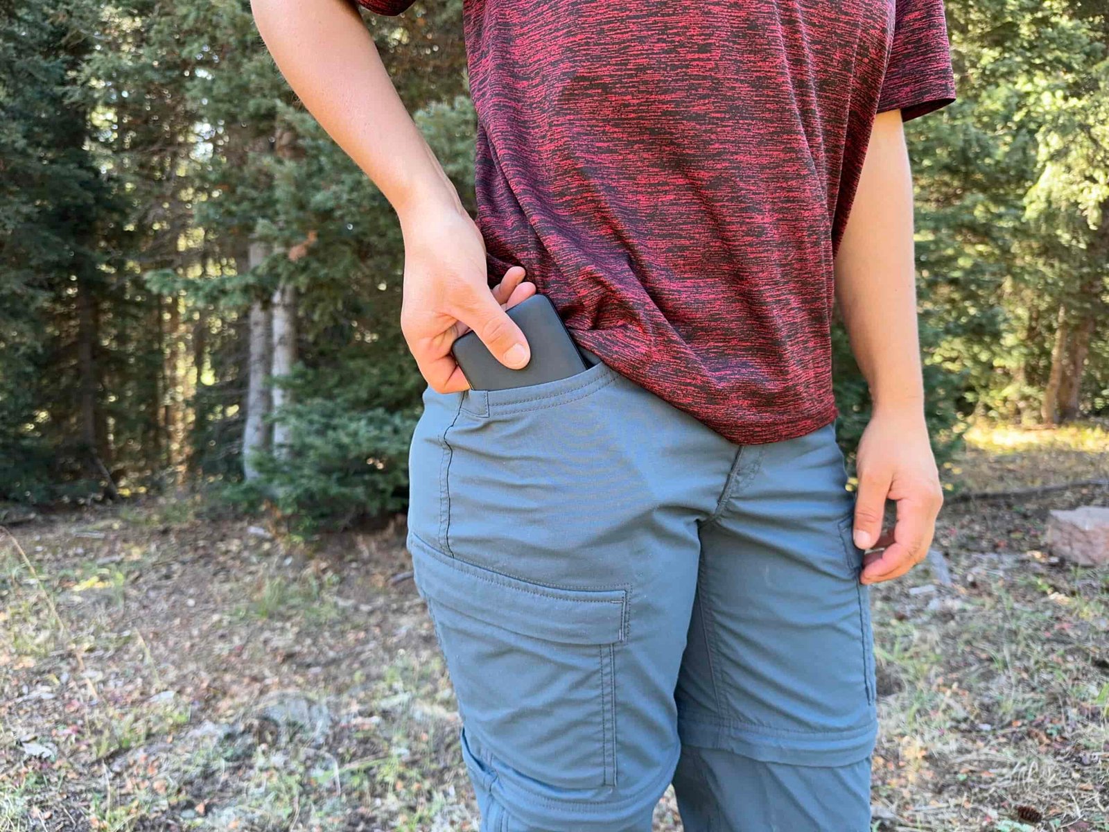 A close up of a person placing a power bank in the hip pocket of the REI Sahara pants.