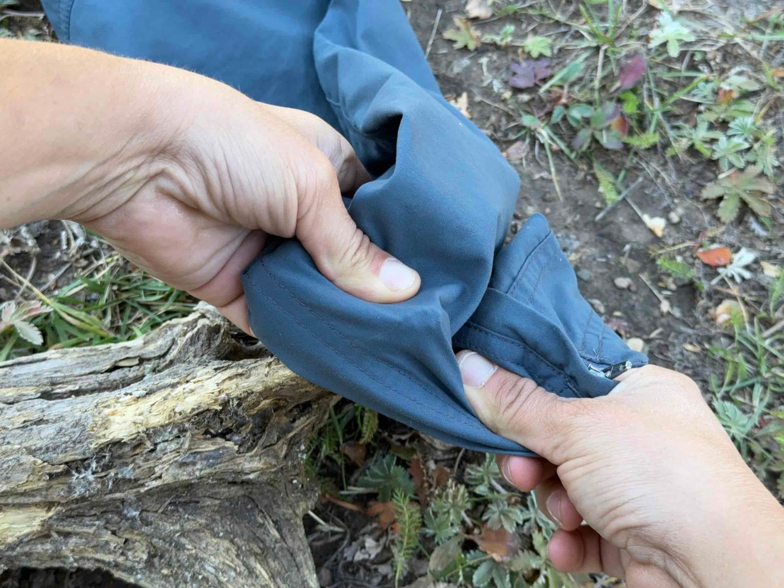 A close up of two hands is stretching the fabric of the REI Sahara pants over a pokey stick to test for durability.