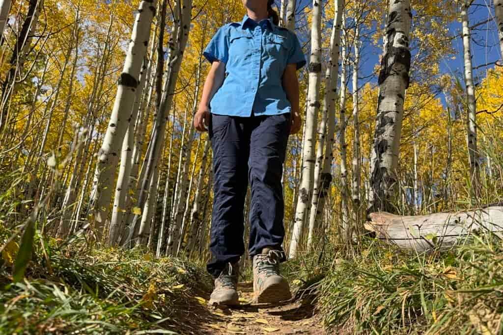 a day hiker wearing the north face aphrodite 2.0 pants on a trail through an aspen forest