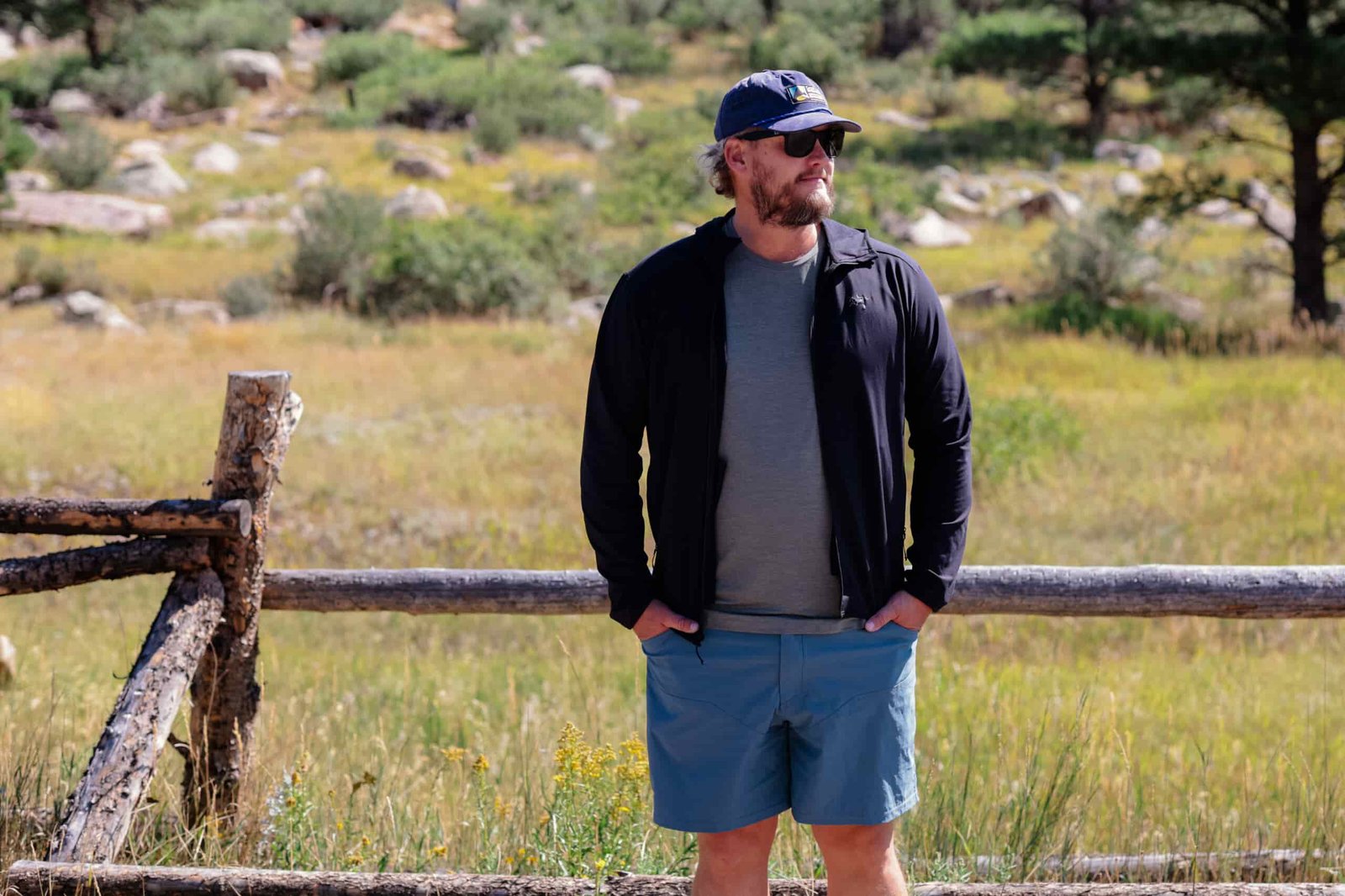 Man stands on trail by a fence.