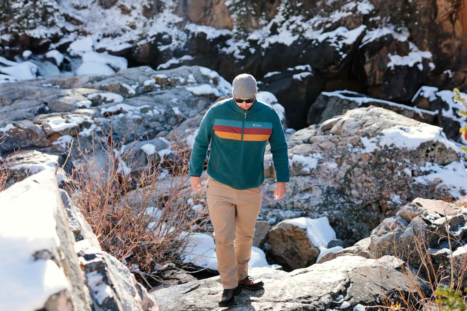 A man walks over a snowy boulder field.