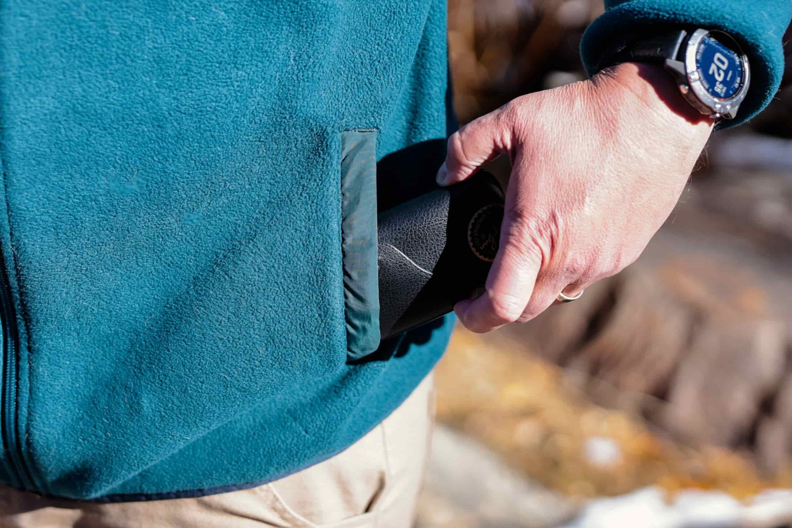 A hand pulls a sunglasses case out of a fleece pocket.