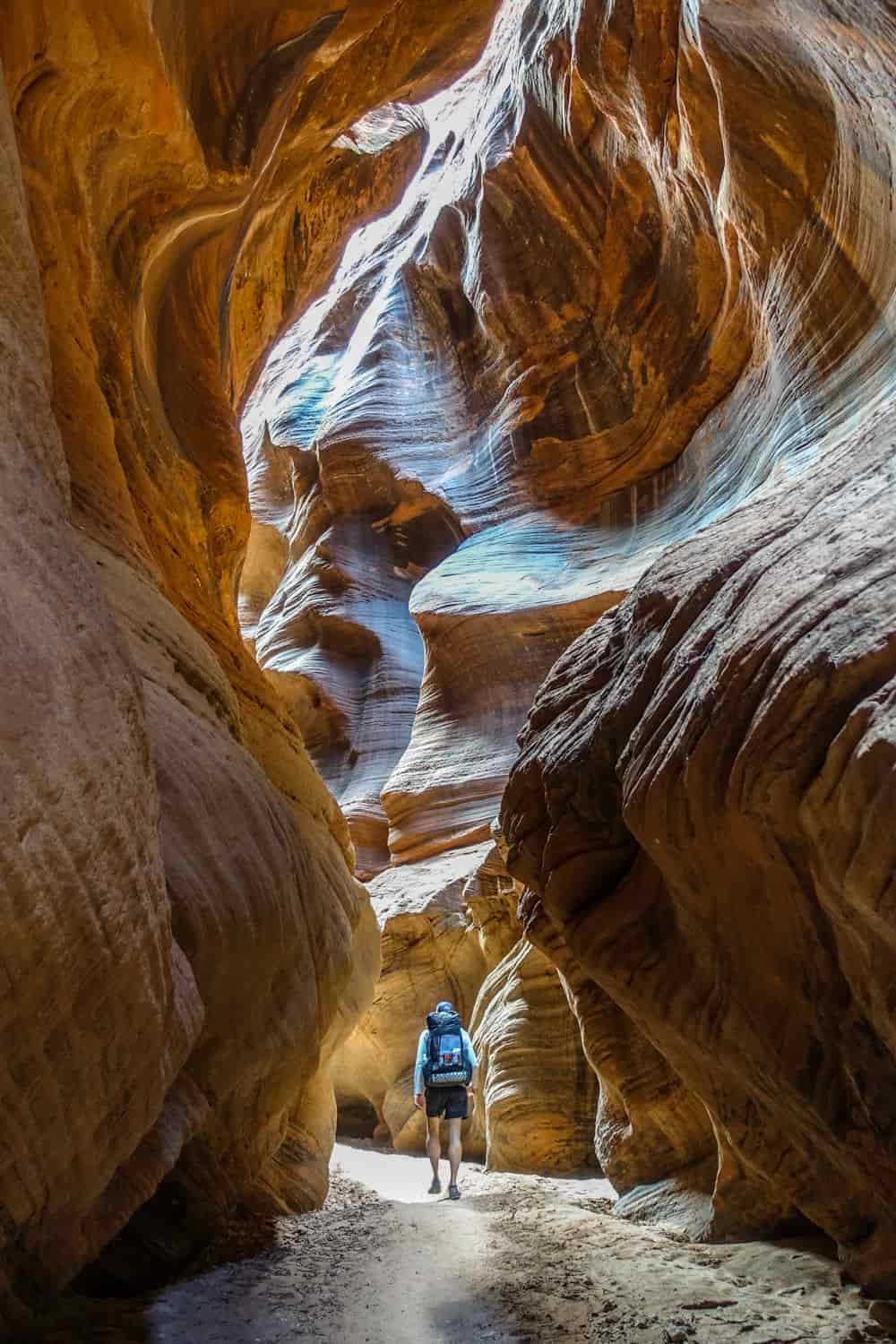 a backpacker heads toward a sunlit section of a slot canyon