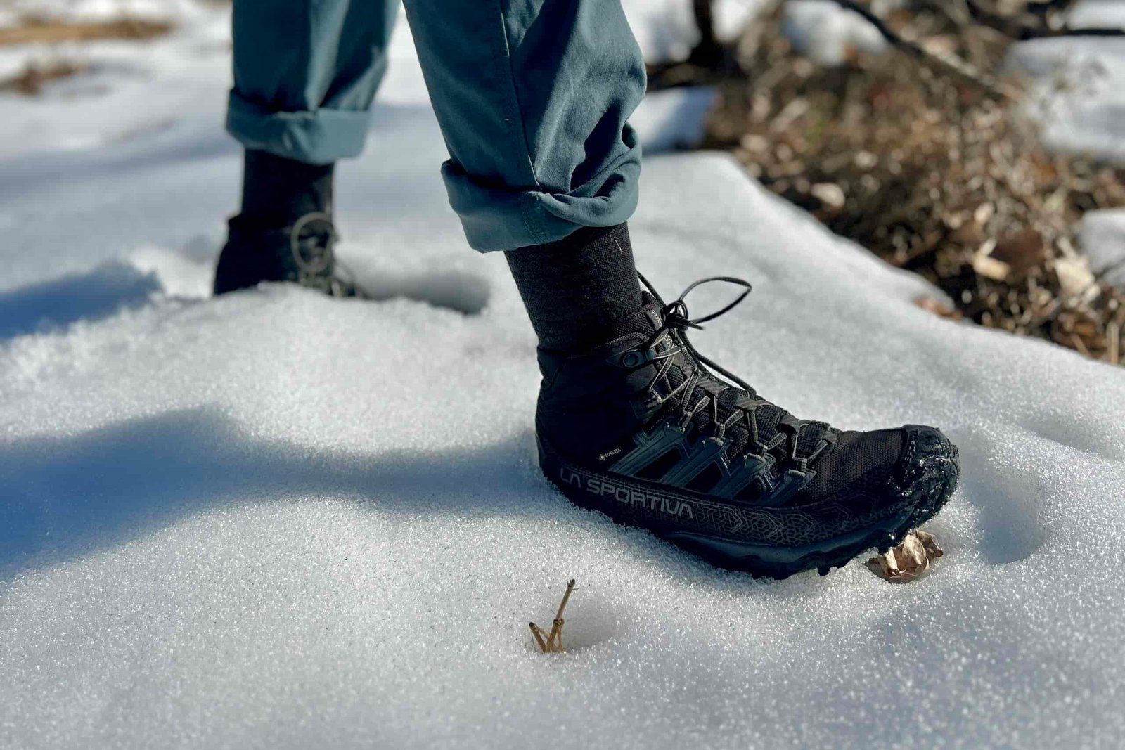Close-up image from the knees down of a person walking in hiking boots in snow.