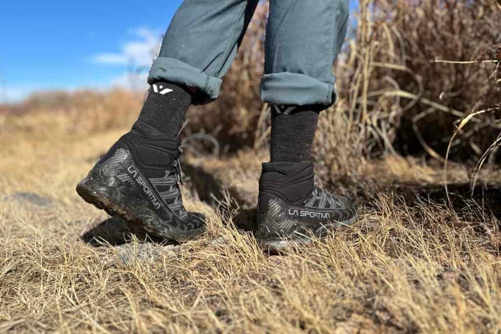 Close-up image from the knees down of a person walking in hiking boots in a wilderness area.