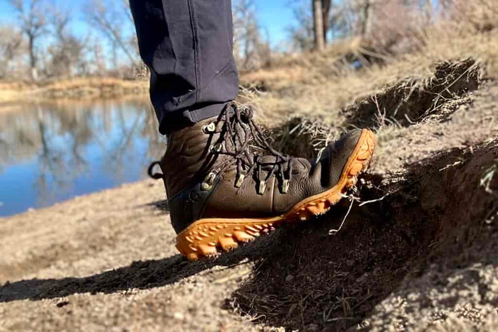 Close up image from knees down of a boot flexing against a slight incline near water.