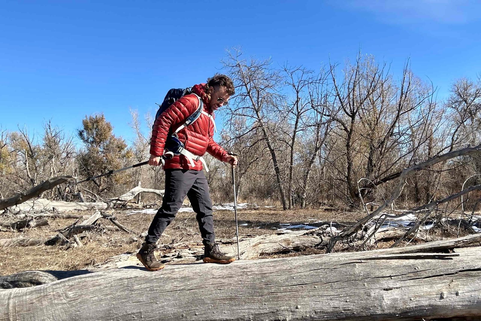 A hiker walks on a log in a wilderness area on a bluebird day.