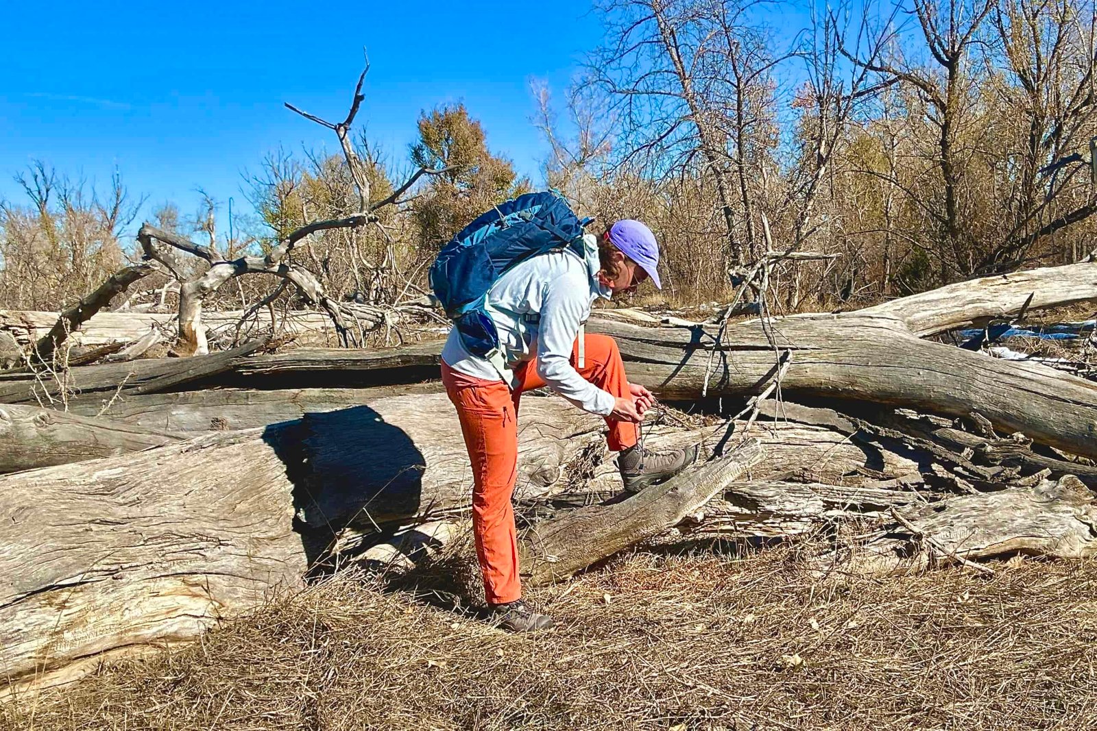 A man ties his shoes while propping his foot up on a log in a wilderness area.