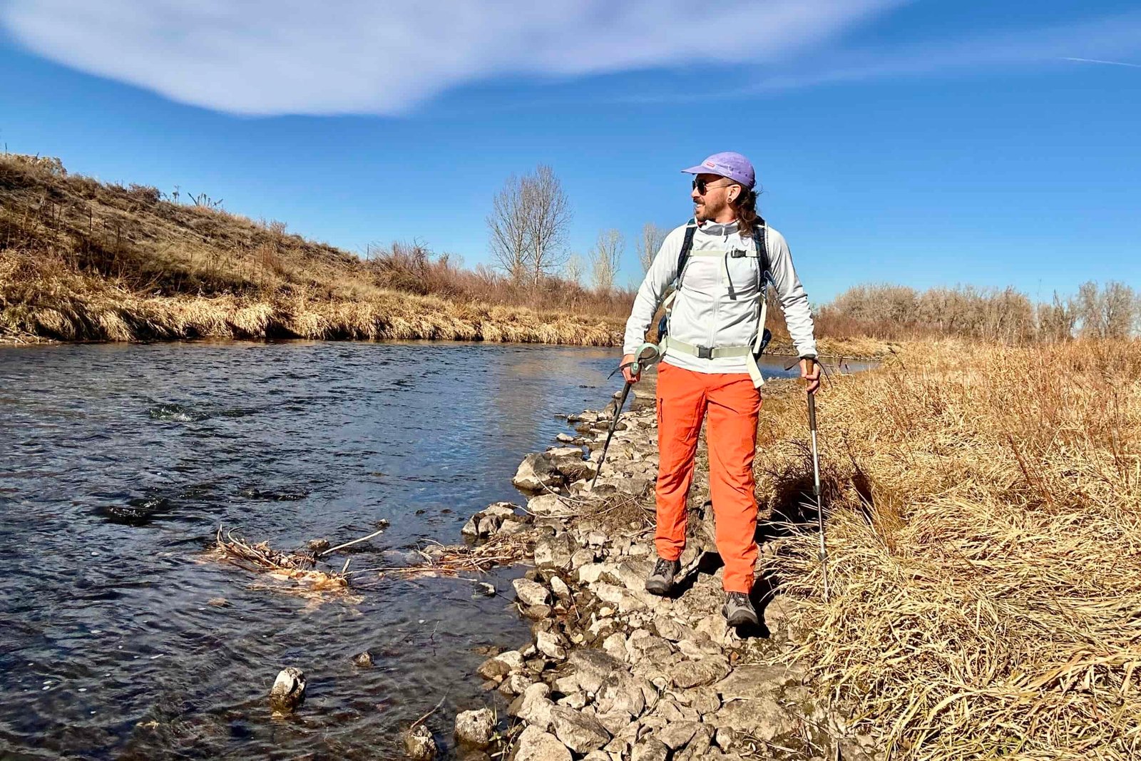 A hiker walks along a river looking off in the distance.
