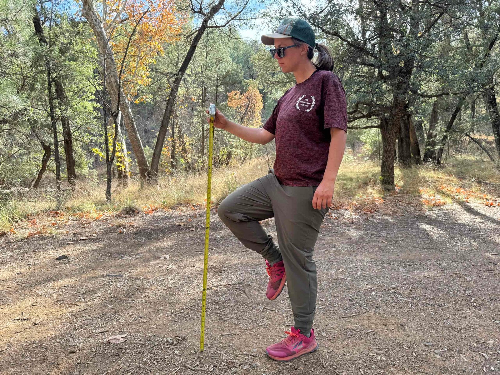 A person stands on one foot while holding the other knee up. A measuring tape is extended next to the raised knee to test for mobility of the Patagonia Happy Hike Pants.