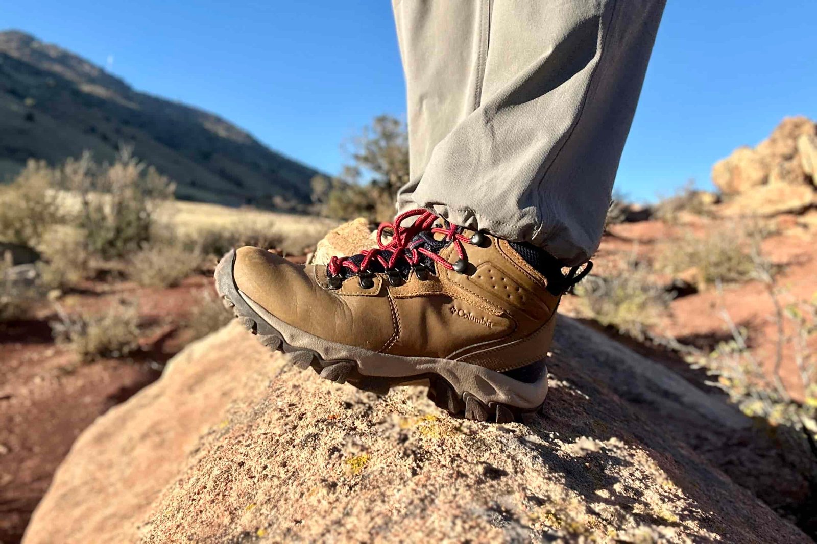 Close up from knees down of a person walking in hiking boots on a rock in the sun.