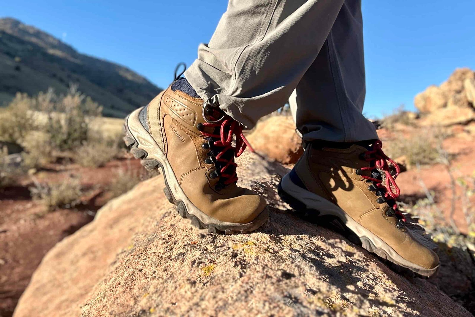 Close up from knees down of a person walking in hiking boots on a rock in the sun.