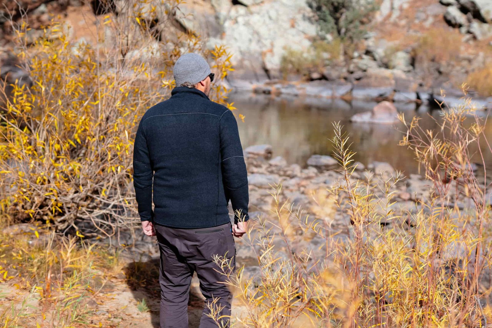 A man walks by a river in fall leaves.