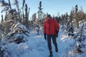 A man walks down a narrow trail in a winter forest.