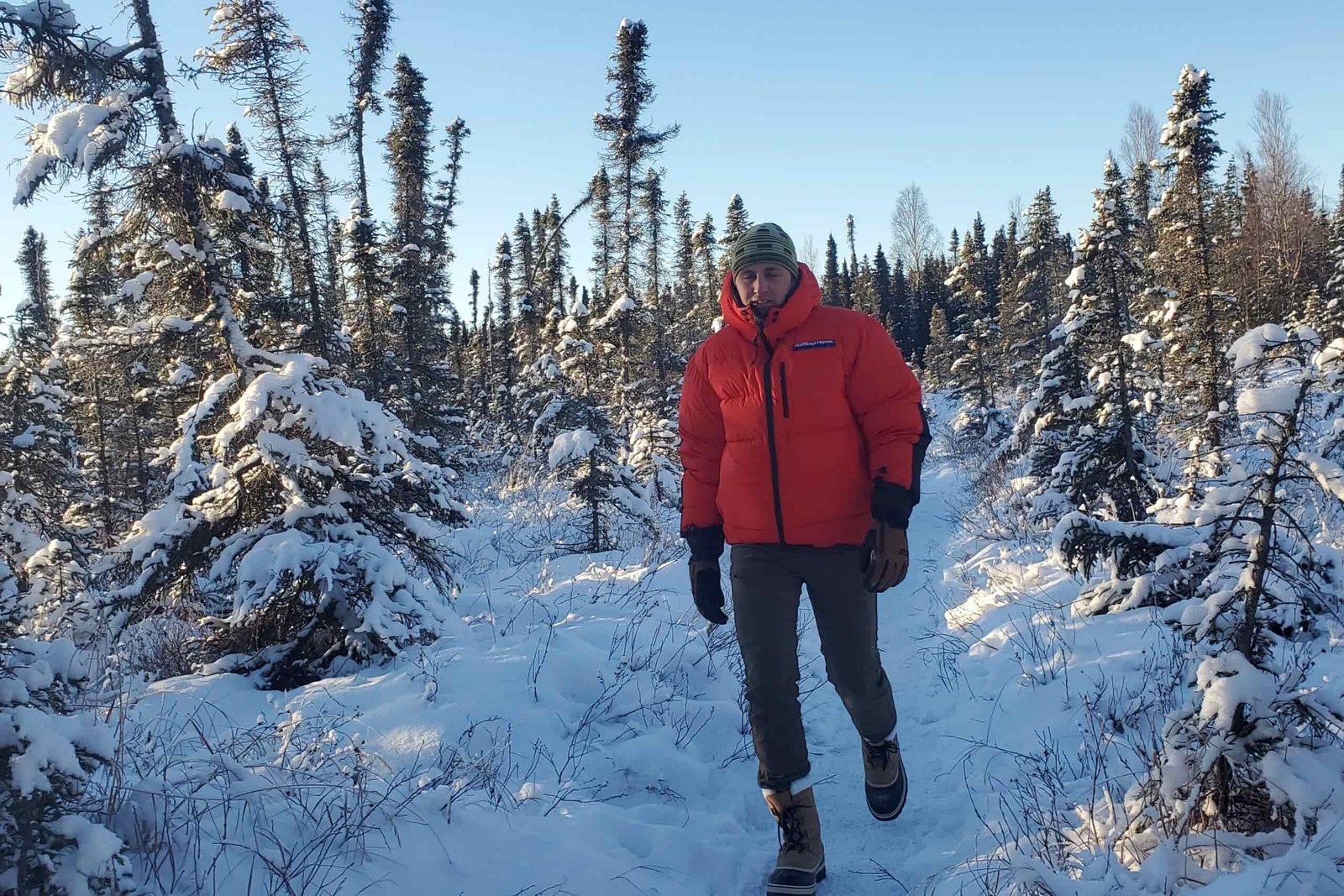 A man walks down a narrow trail in a winter forest.