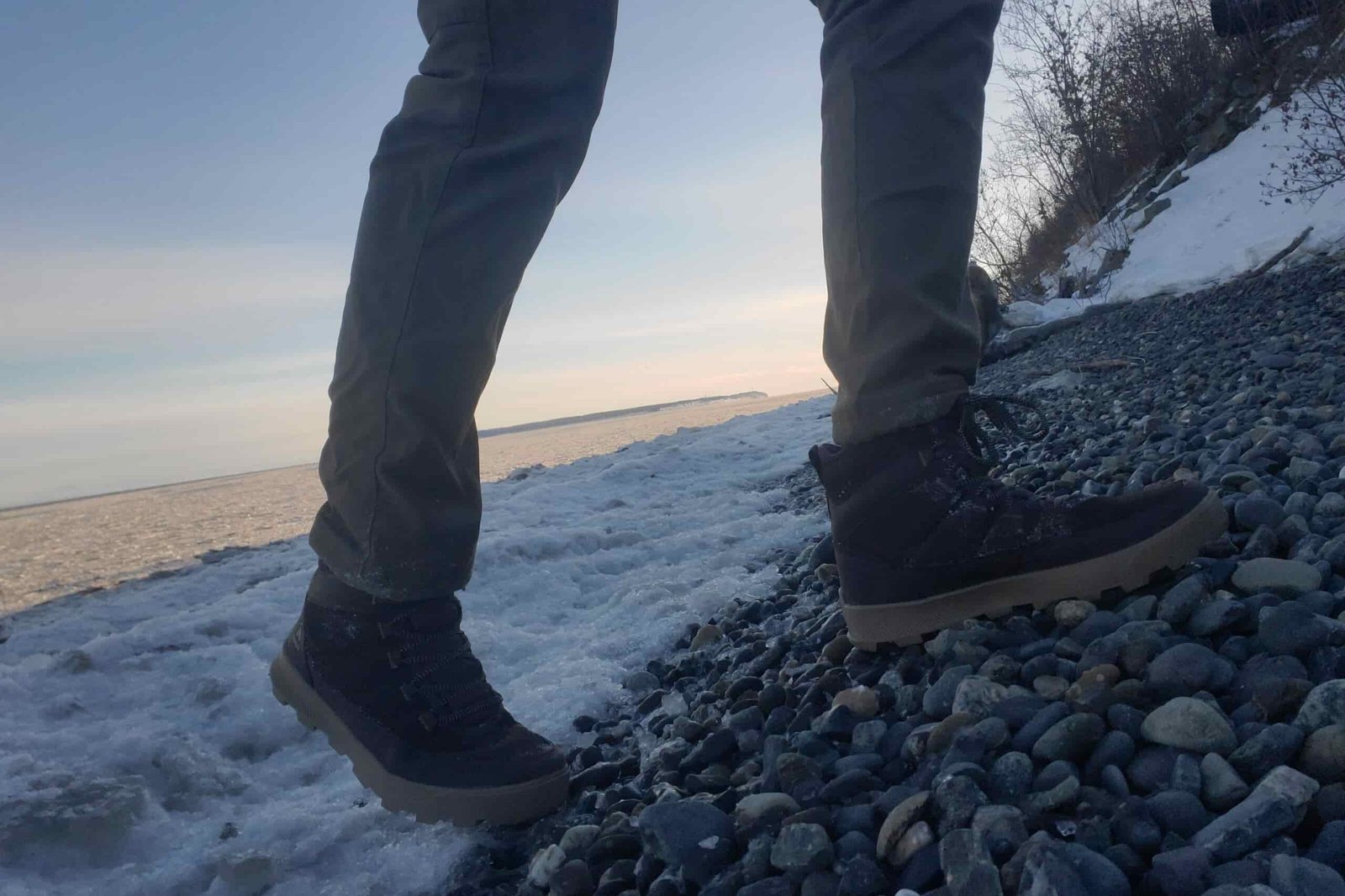 A closeup of boots walking up ice covered rocks.