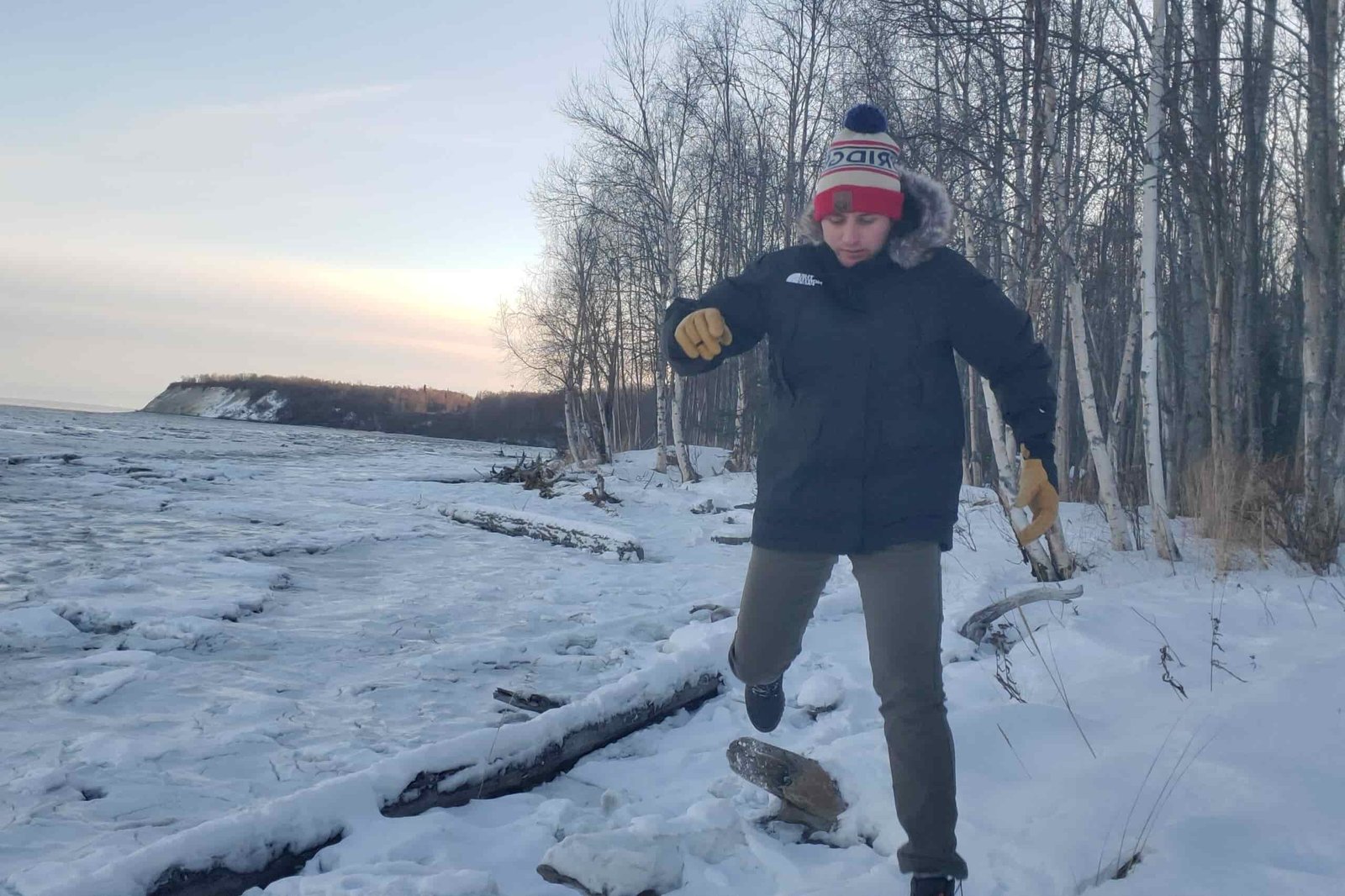 A man steps off a long on a snowy shoreline.