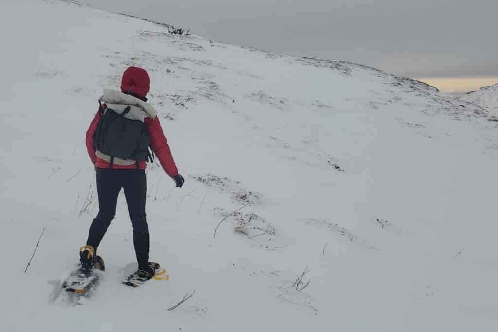 A woman walks across snowy alpine wearing snowshoes.