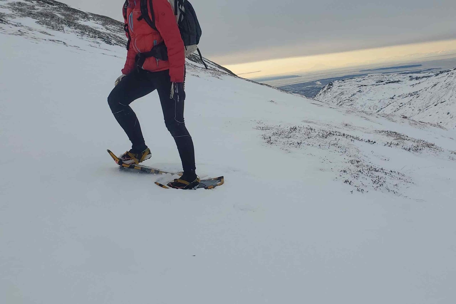 A woman walks up a mountainside wearing snowshoes.