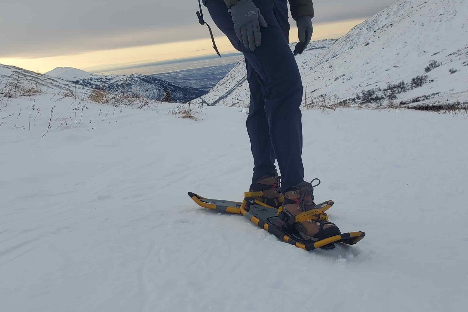 A person standing on a snowy mountainside wearing snowshoes.