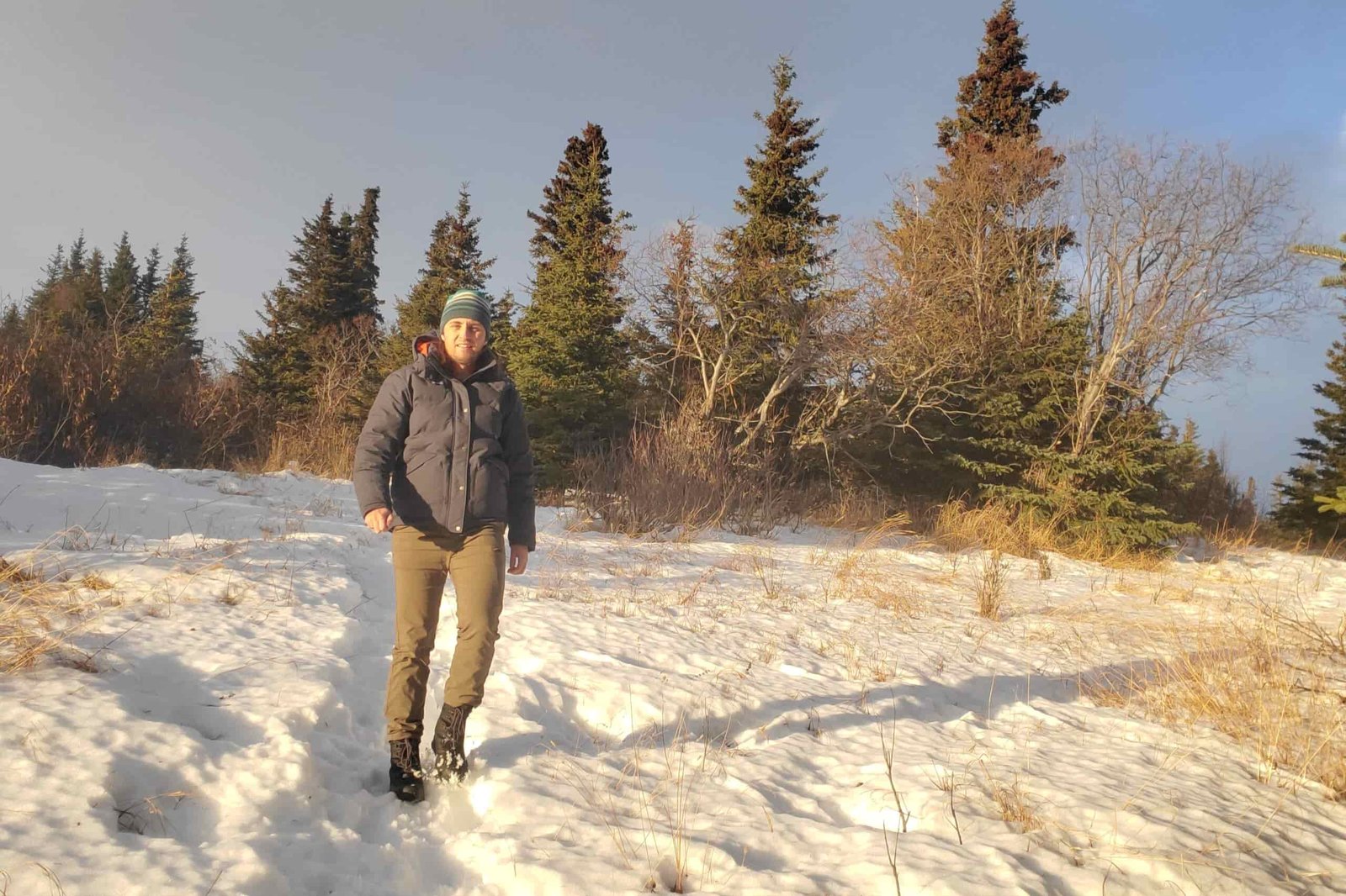 A man walks down a snowy trail in sunlight.