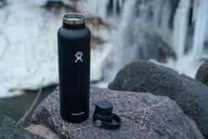 The Hydro Flask Standard Mouth, with its lid off, sits on a rock with a partially frozen waterfall in the background.