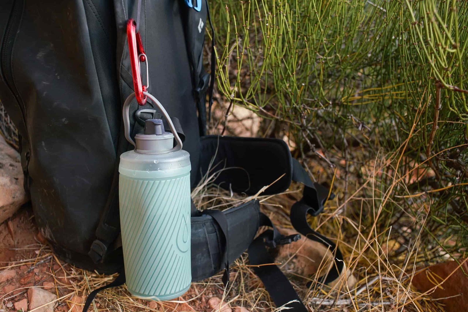 The Hydrapak Flux water bottle is clipped via a carabiner onto a backpack.