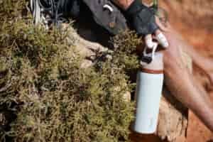 A person wearing crack climbing gloves and with taped fingers holds the Owala FreeSip Vacuum Insulated water bottle by its carrying handle.