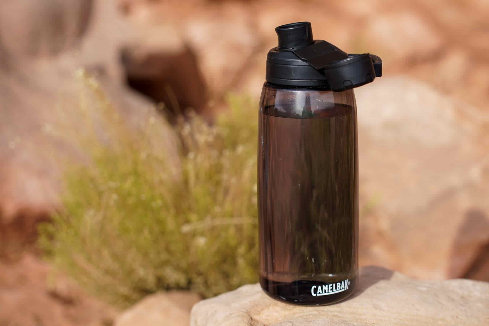 The CamelBak Chute Mag Renew water bottle sits on a rock with a sage brush and rocks in the background.