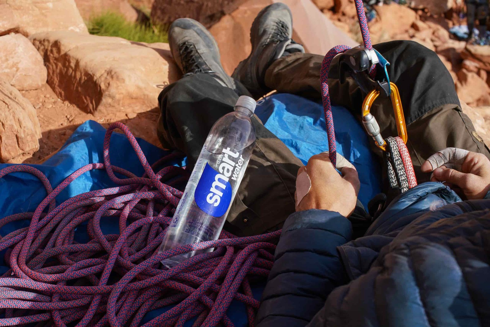 A bottle of Glaceau Smartwater rests on a pile of rope beside a person belaying an unseen climber.