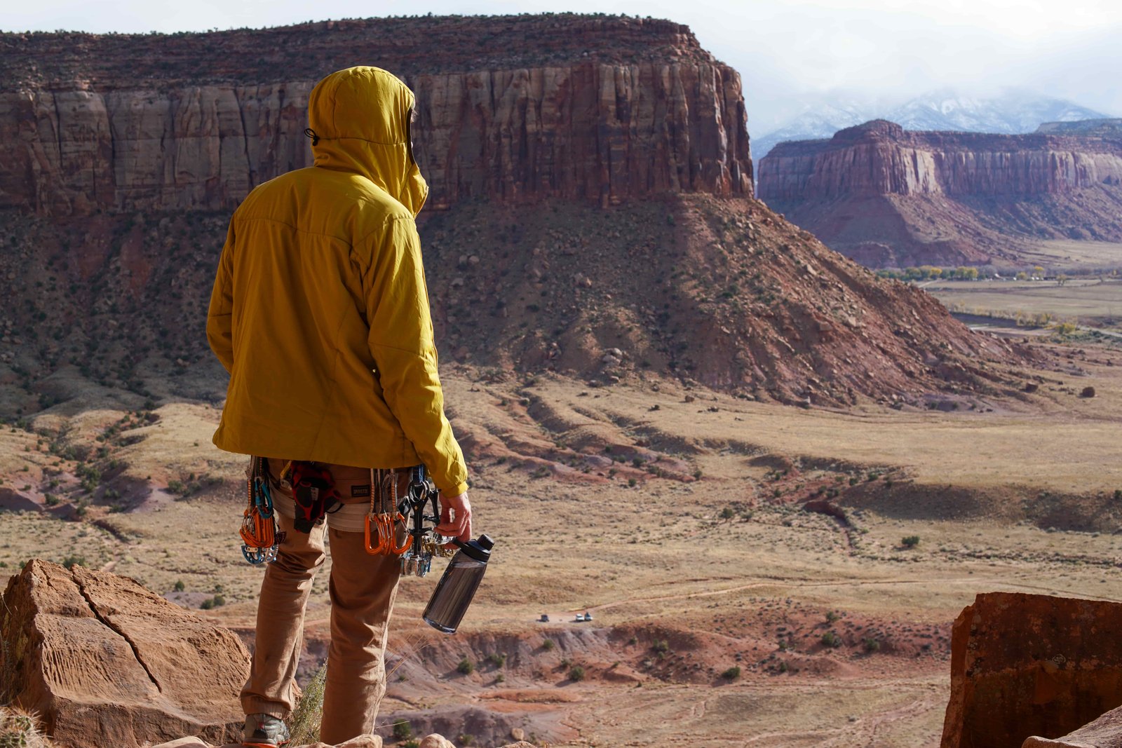 A person wearing a climbing harness holds the CamelBak Chute Mag Renew water bottle in their hand with a wide canyon expanse in the background.