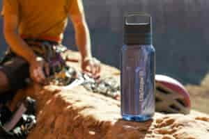 The LifeStraw Go Series water bottle sits on a rock with a climber sorting their gear in the background.