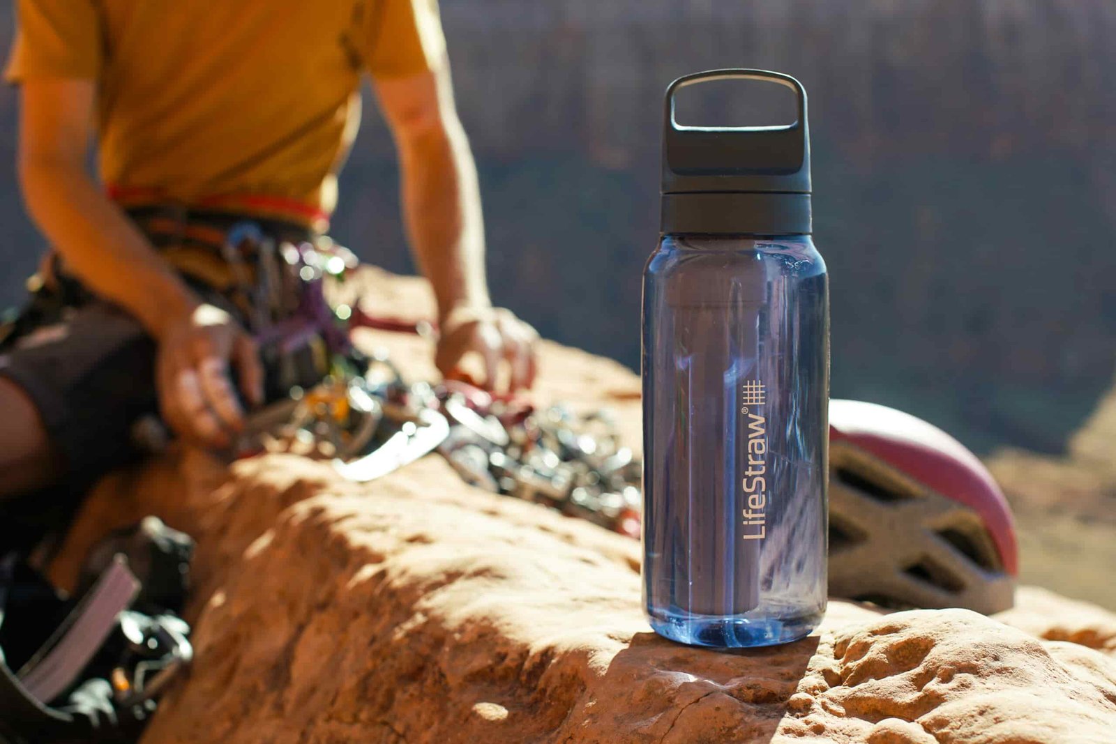 The LifeStraw Go Series water bottle sits on a rock with a climber sorting their gear in the background.