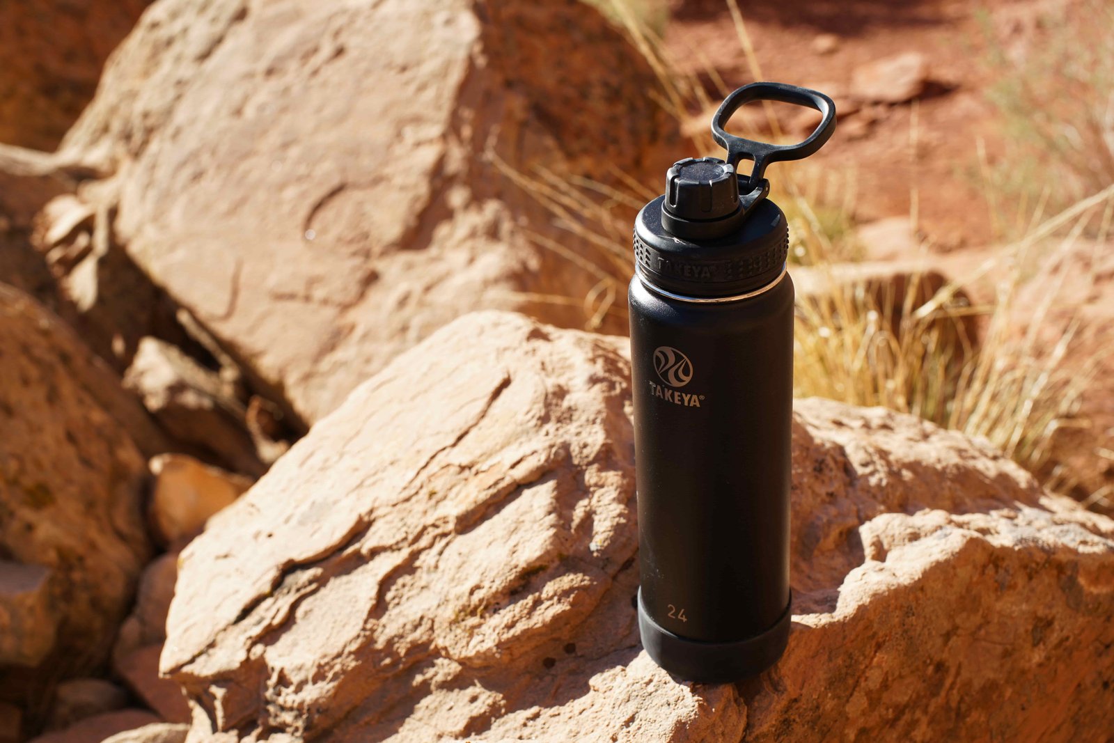 The Takeya Actives Insulated water bottle sits on a rock.