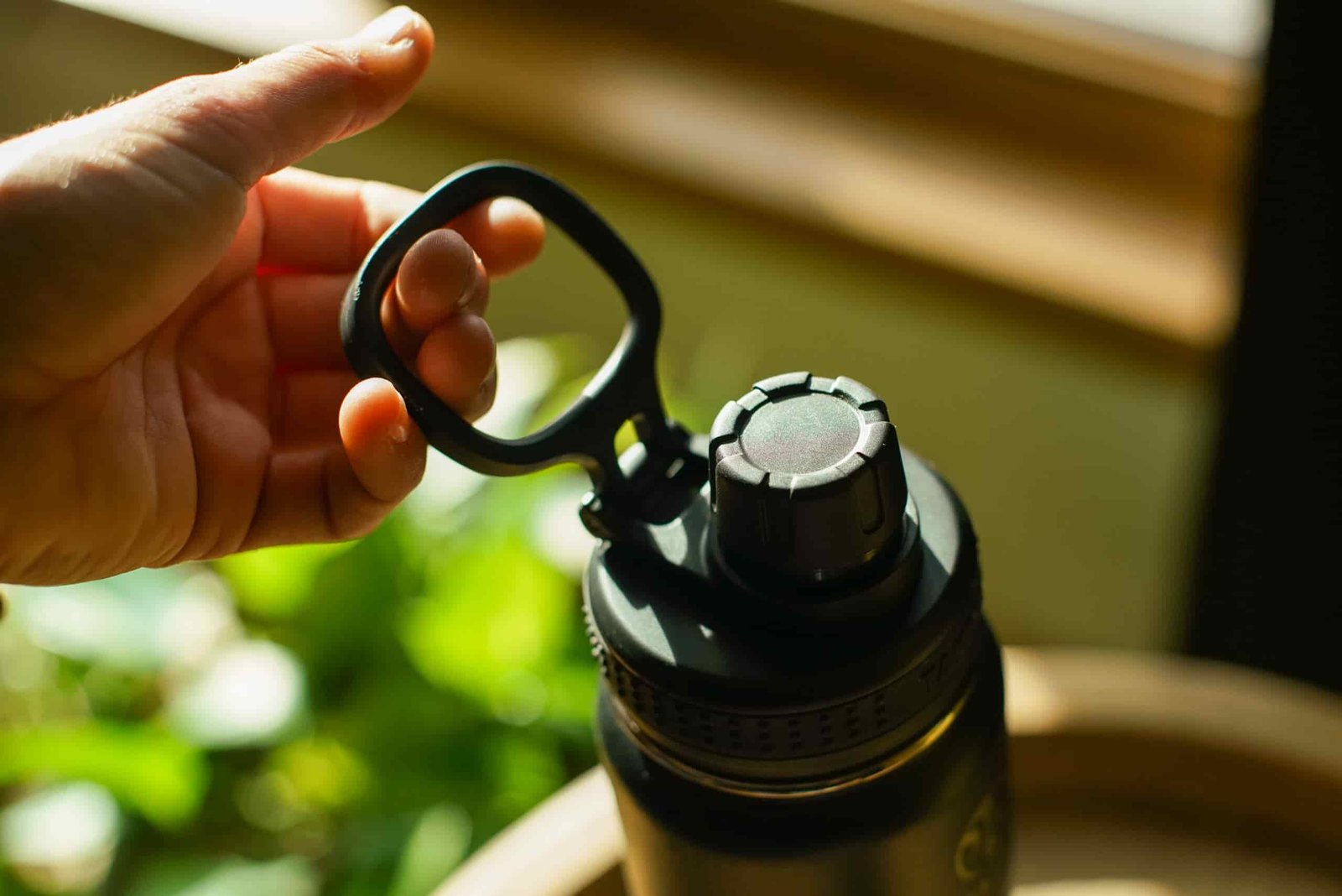 A close up of a person's hand holding the Takeya Actives Insulated water bottle's carrying handle.