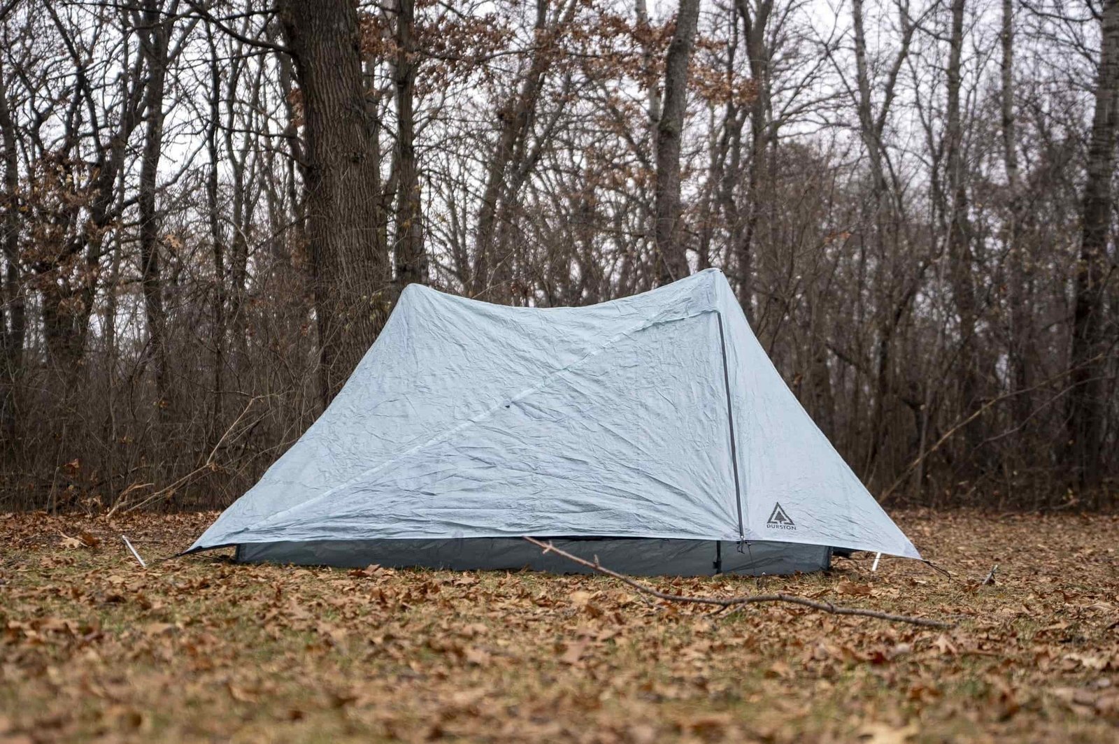 a trekking pole tent with doors zipped up in a forest clearing