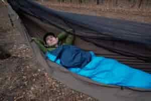 a man in a blue sleeping bad lays in a green hammock
