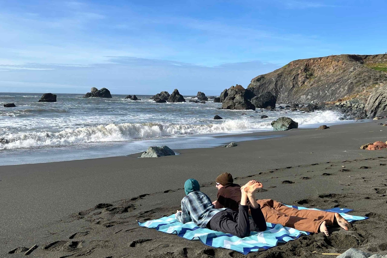 2 people lay in on their stomaches on the large size of the CGear Multimats Sandlite Sand-free Mat at the beach.
