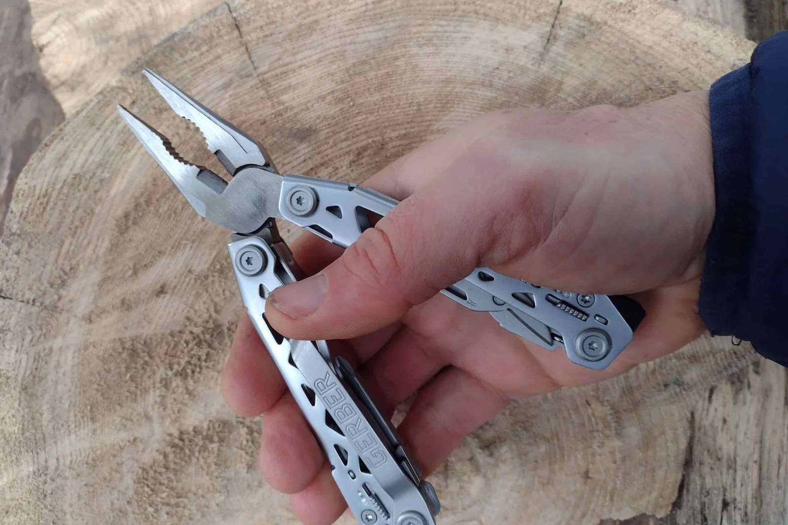 The silver Gerber Suspension NXT held above a log.