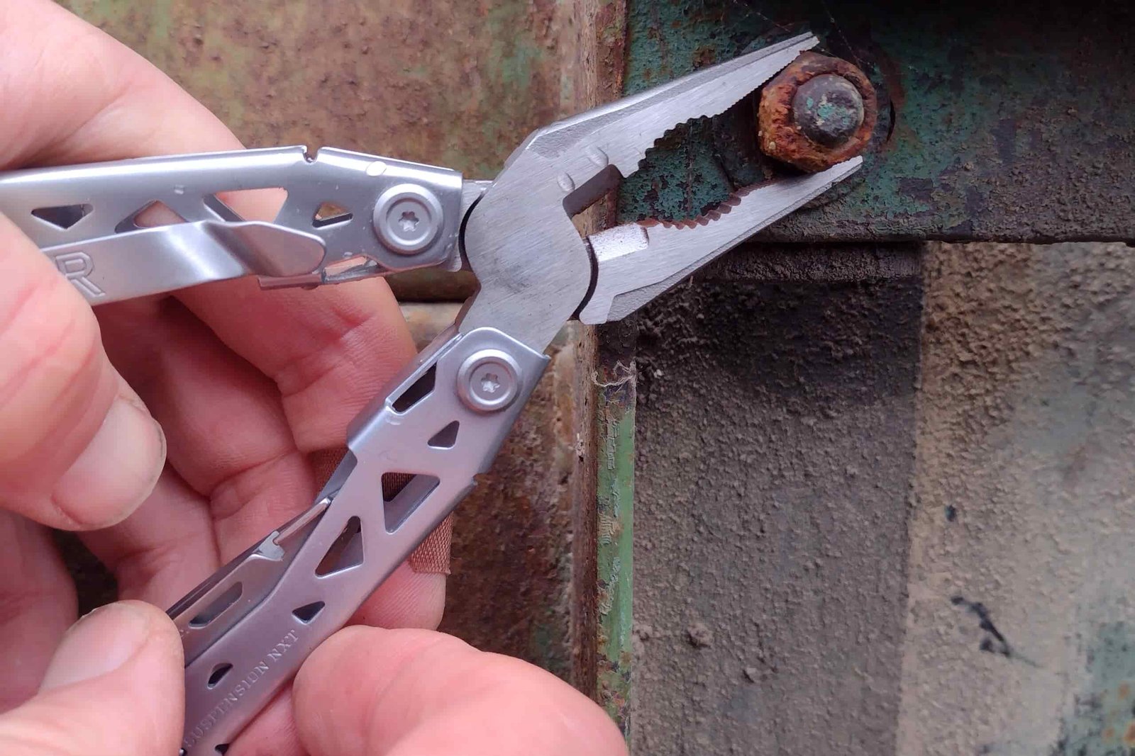 The silver Gerber Suspension NXT gripping a rusty nut with its needle nose pliers.
