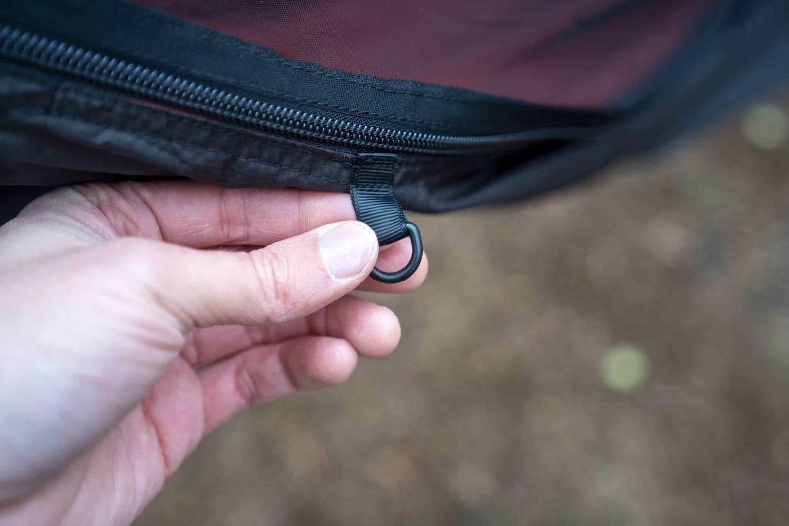 a hand holds a d ring on the exterior of a hammock