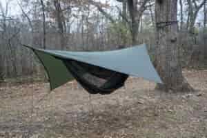 a green hammock with a green tarp in a forest clearing