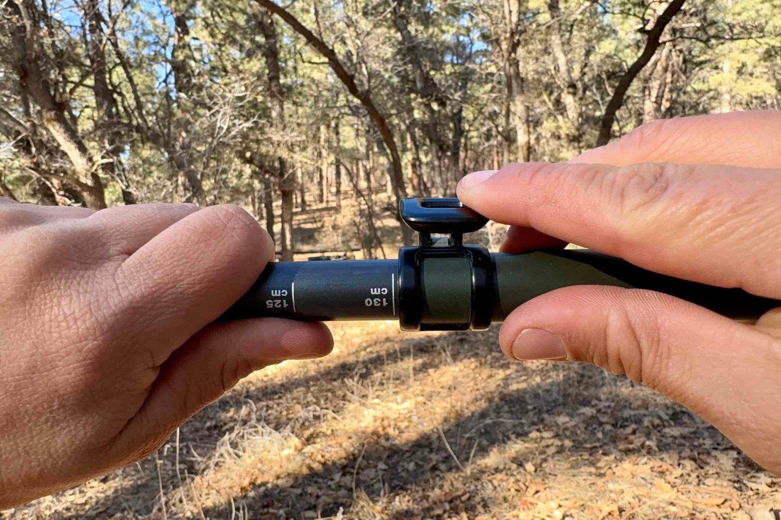A close up of a hand closing a flick lock with trees in the background.