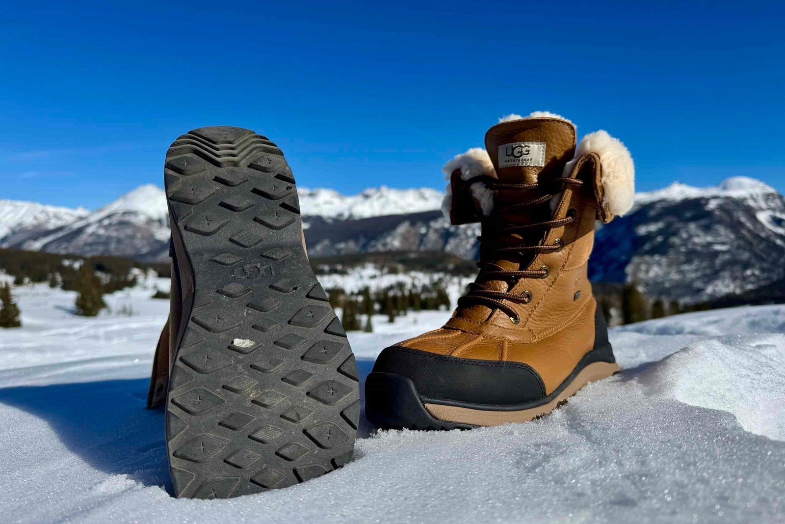 A close up of the tread on the bottom of the UGG boot. It is sitting in the snow in the mountains.