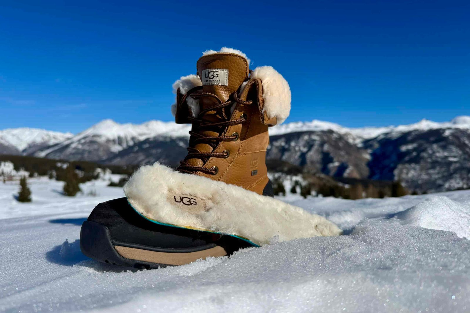 A close up of the UGG boot with the insole sitting next to it. They are set on some snow in the mountains.