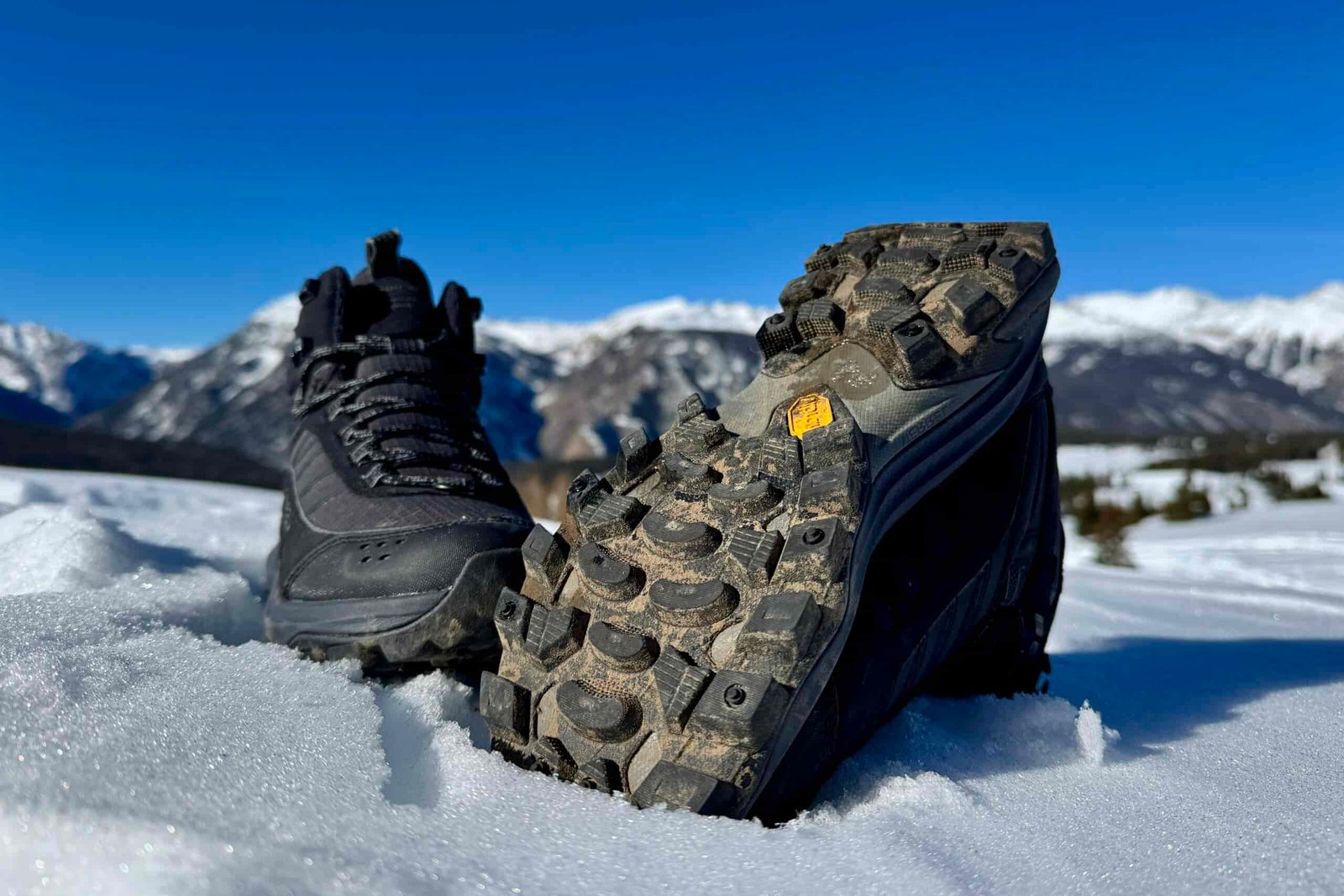 A close up of the tread on the bottom of the Merrell boot. It is sitting in the snow in the mountains.