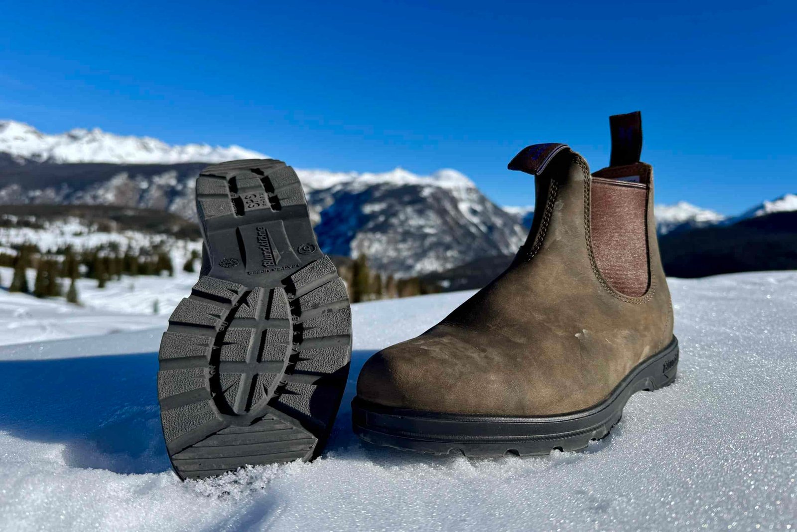 A close up of the tread on the bottom of the Blundstone boot. It is sitting in the snow in the mountains.