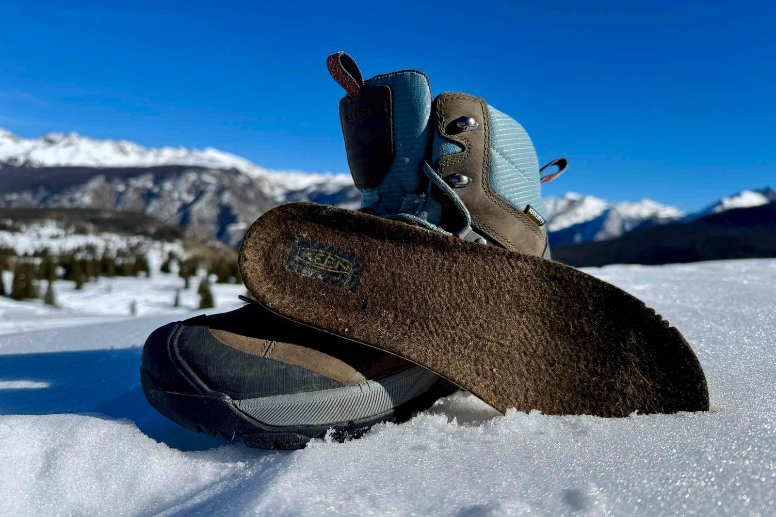 A close up of the Keen boot with the insole sitting next to it. They are set on some snow in the mountains.