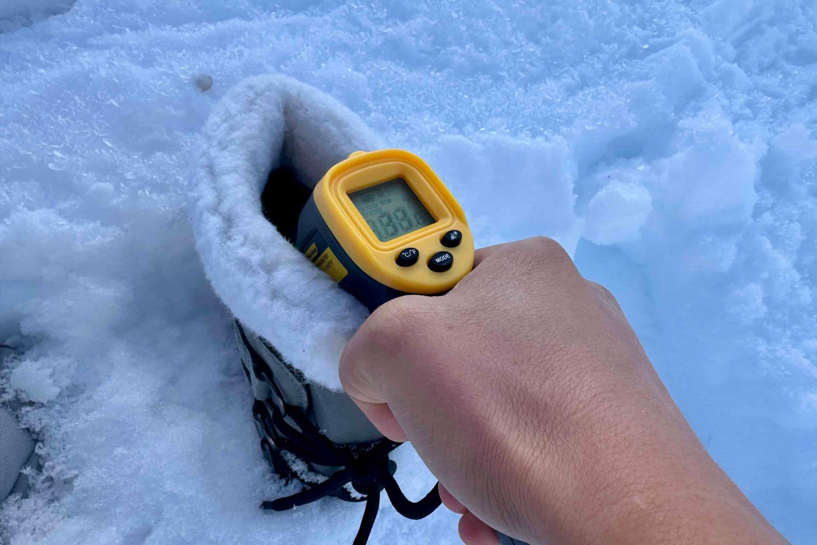 Close up of a hand pointing a laser thermometer into the Sorel boot which is sitting in the snow.